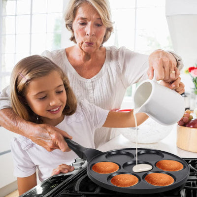 mamie et enfant preparant des crepes dans crepiere a 7 trou sur gazinière a gaz