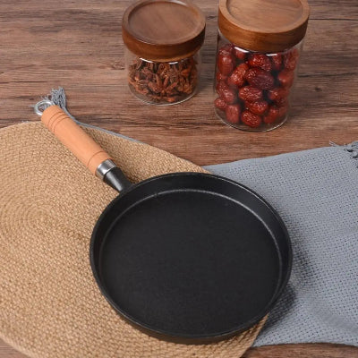 poele a crepes en fonte rebord plat sur dessous en osier sur table en bois avec pots de fruits seches
